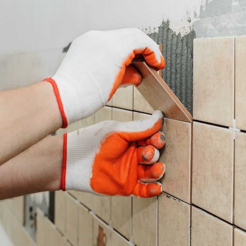 manos de albañil colocando azulejo en baño